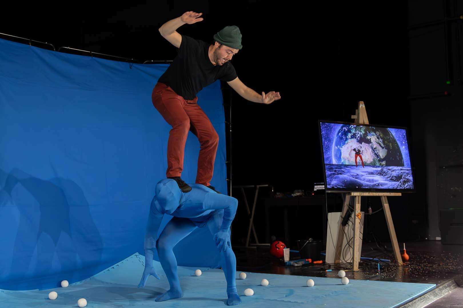 Un acrobate est juché sur le dos d'un autre devant un écran bleu